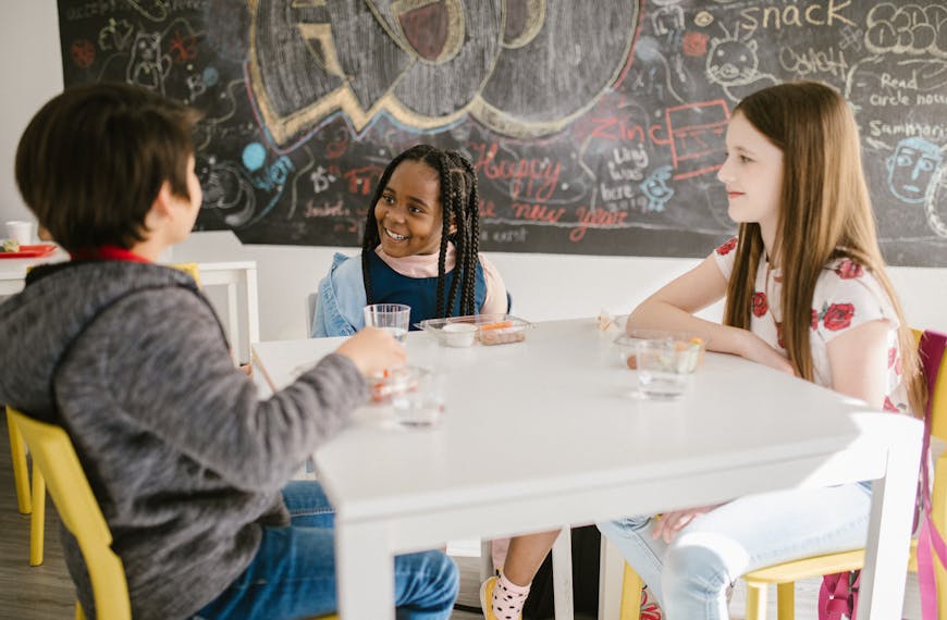 Three children engage in lively conversation during snack time at school.