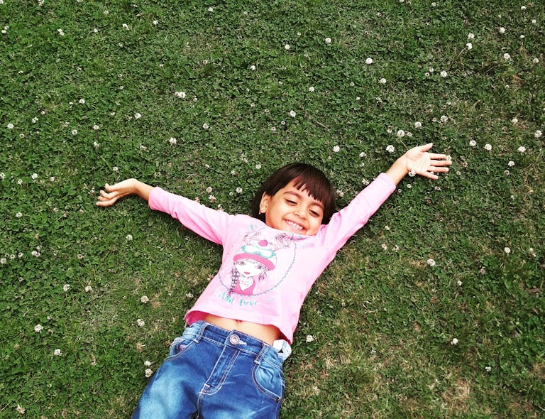 Happy child enjoying a carefree moment lying on grass, arms wide open.