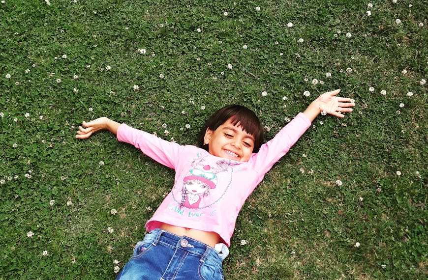 Happy child enjoying a carefree moment lying on grass, arms wide open.